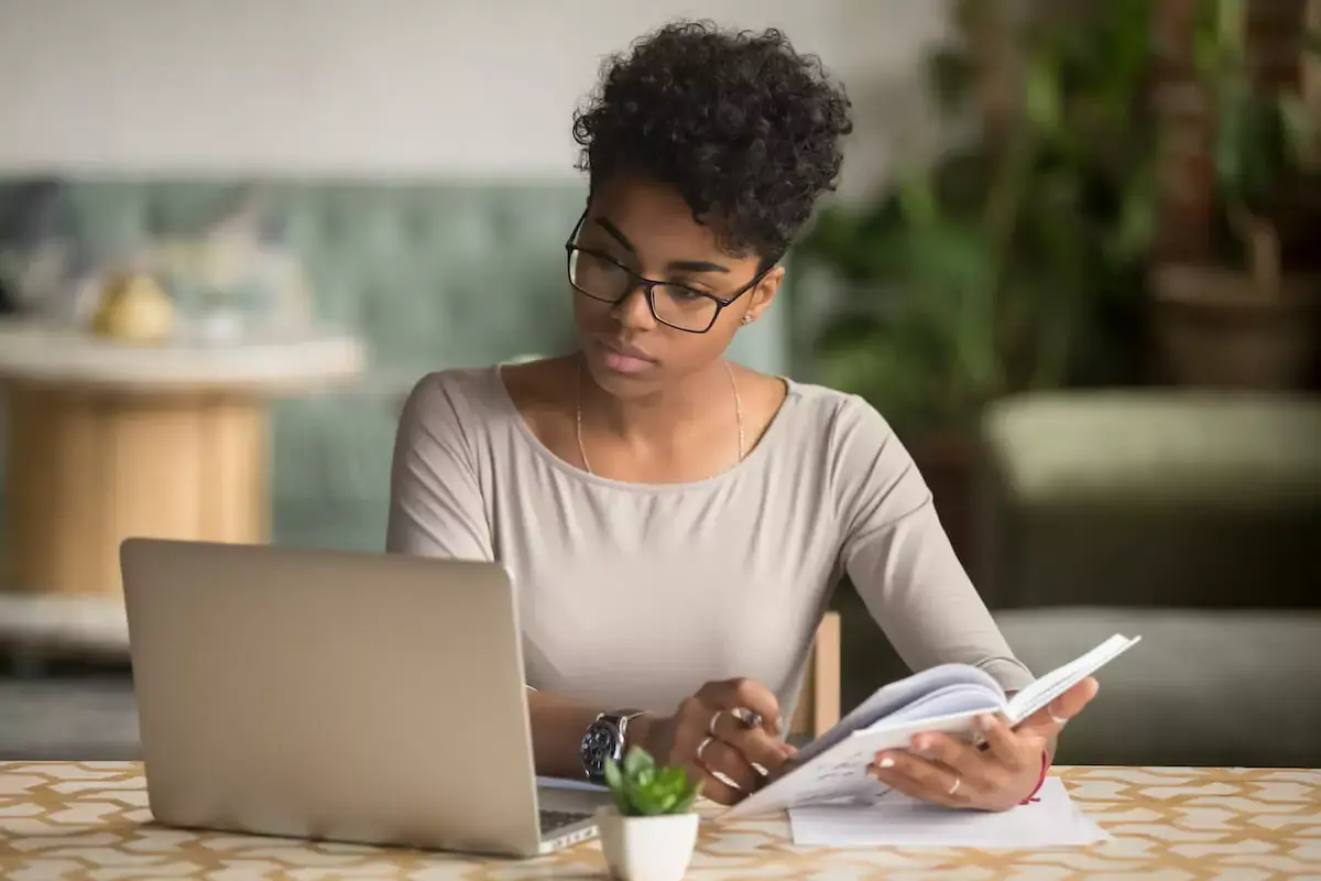 Woman-holding-a-notebook-while-looking-at-her-laptop-screen.jpg