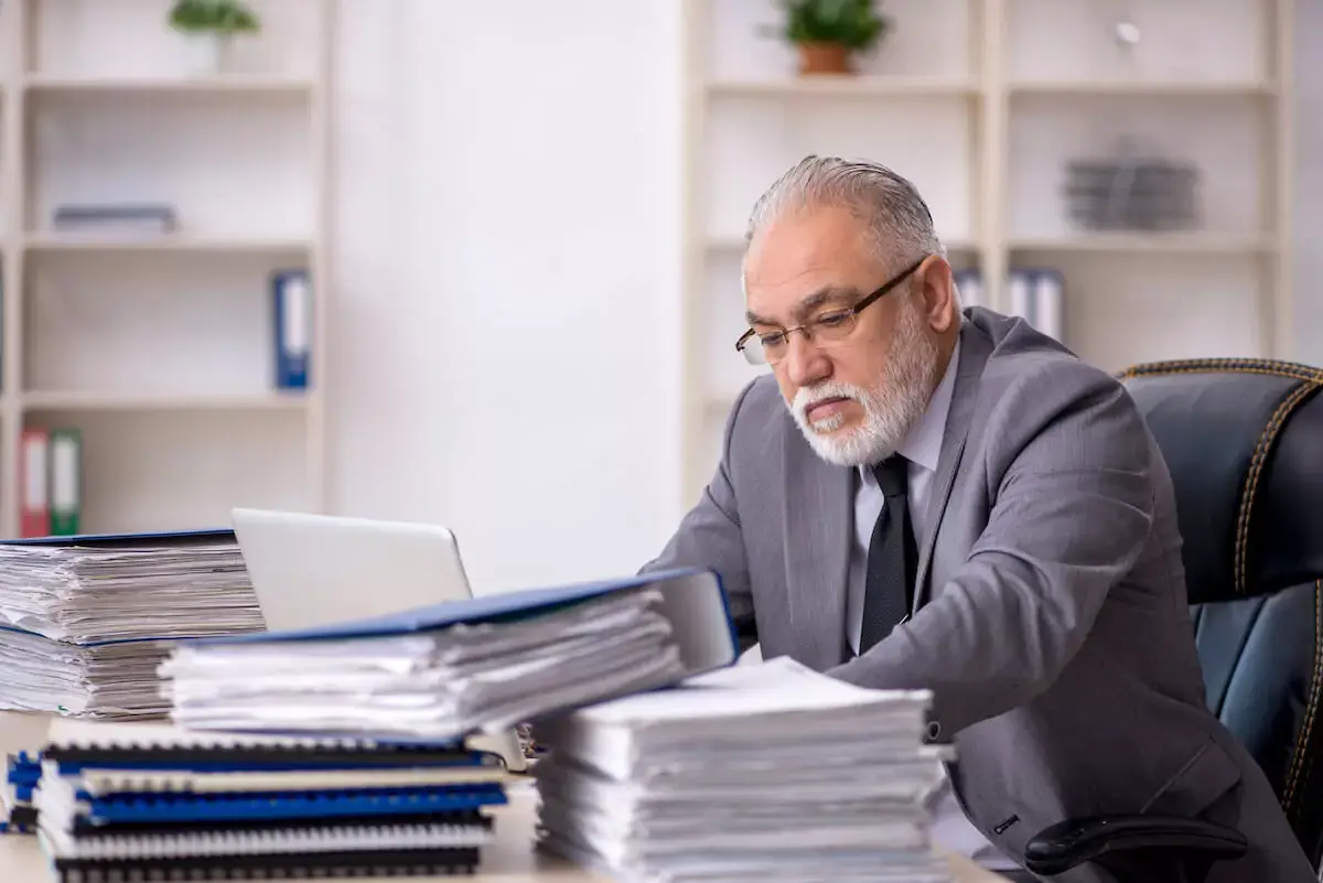old-employee-with-stacks-of-documents-on-his-desk.jpeg