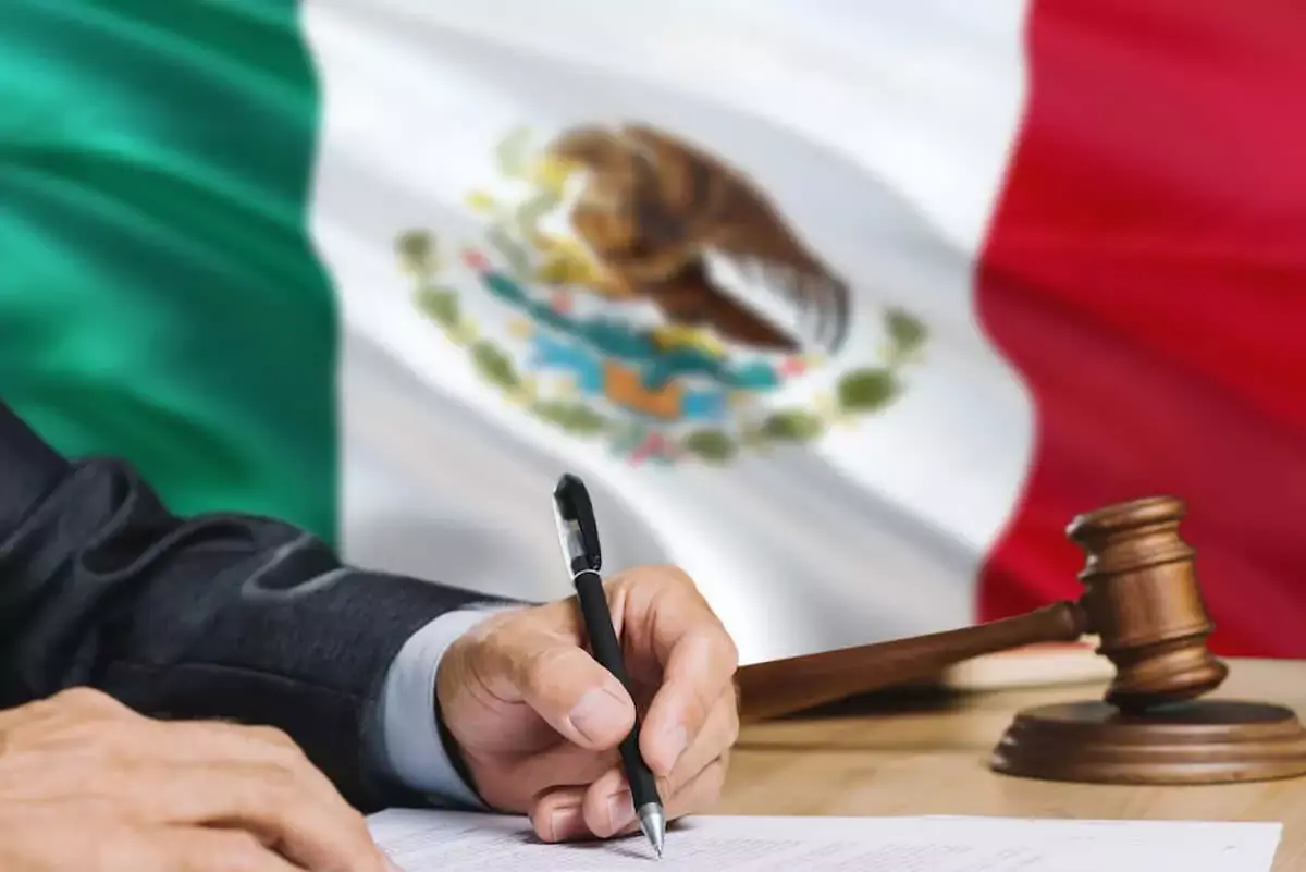 person-writing-on-a-contract-with-the-Mexican-flag-behind-him.jpeg