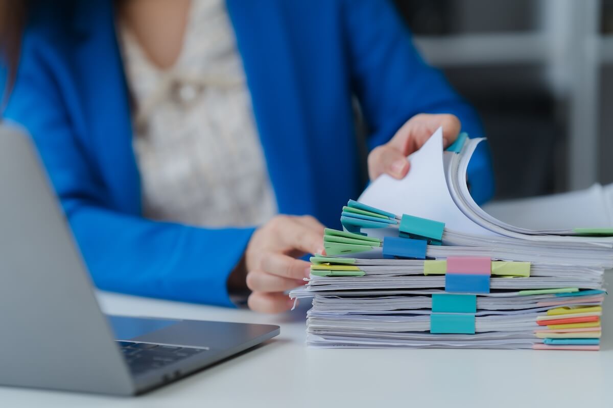 Woman sits at a desk and flips through a stack of documents
