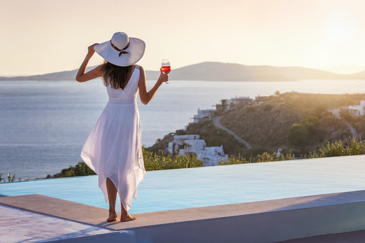 RCI points: woman in a sunhat, holding wine, looking over the sea