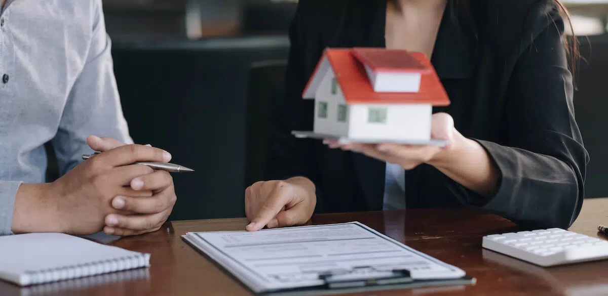 Refinance timeshares: agent holding a miniature house while pointing to a document