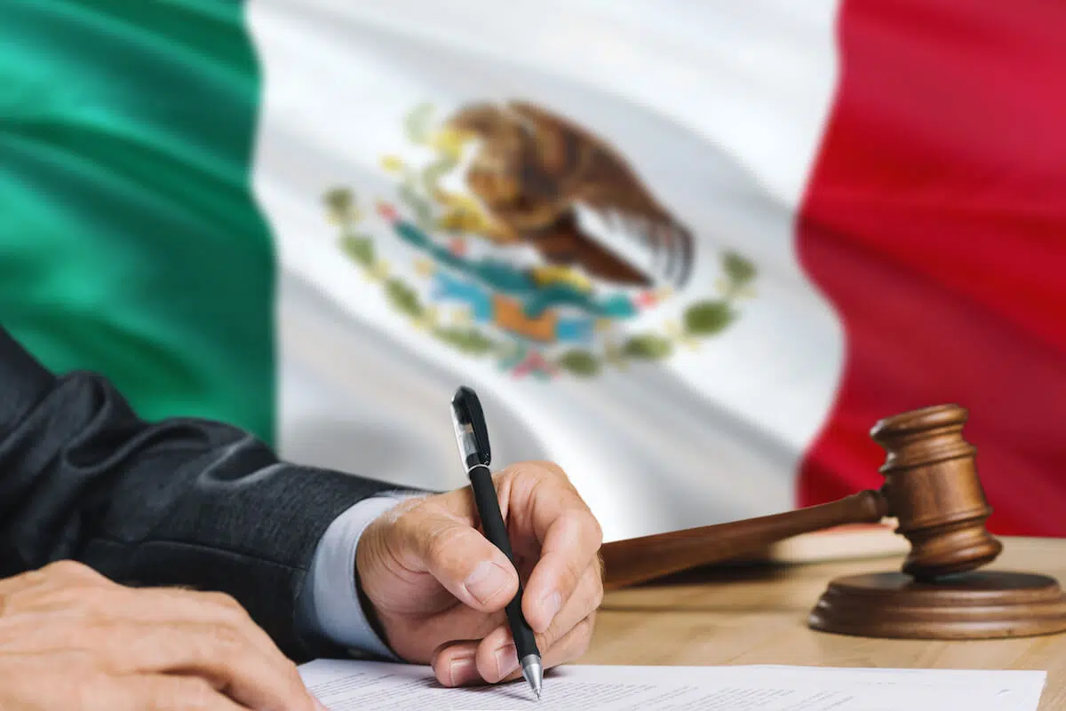 Person writing on a contract with the Mexican flag behind him