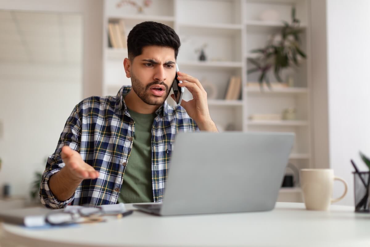 Angry man talking on the phone while looking at his laptop