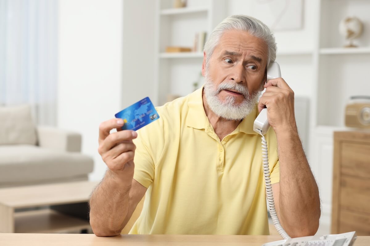 How to Avoid Timeshare Exit Scams: senior man talking on the telephone while holding his credit card