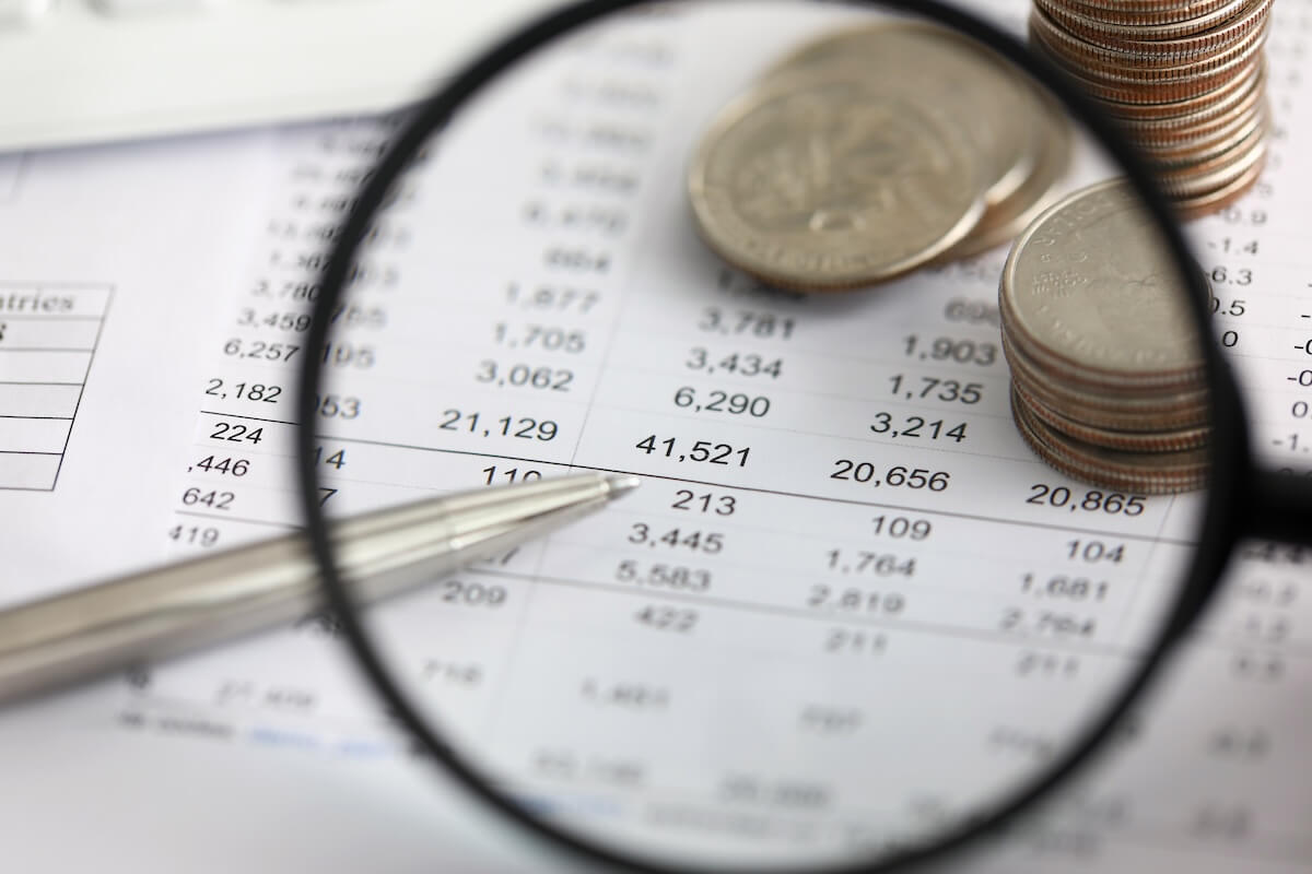 Using a magnifying glass to view some coins, a pen, and a document