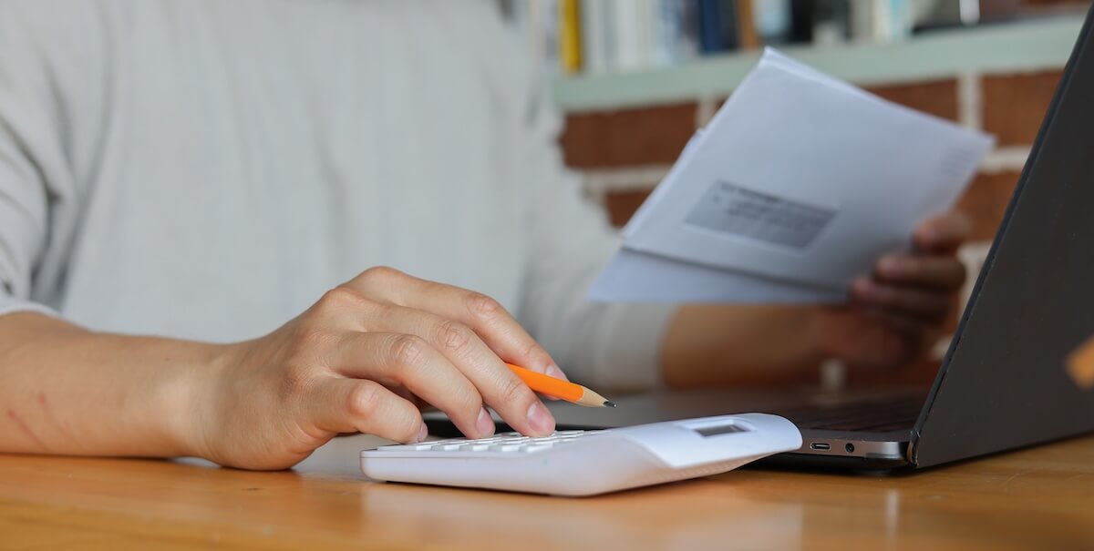 Person using a calculator while holding an envelope